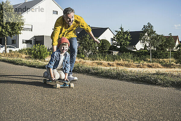 Fröhlicher Mann schiebt Enkel an sonnigem Tag auf Skateboard