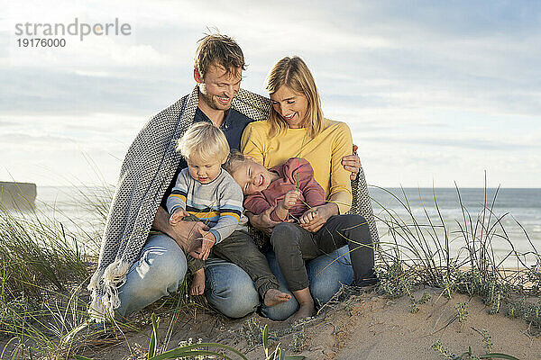 Glückliche Familie mit Decke am Strand sitzend