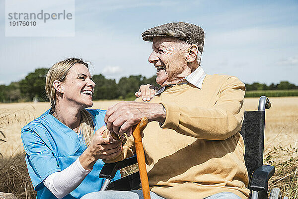 Krankenschwester und älterer Mann mit Behinderung lachen an sonnigem Tag