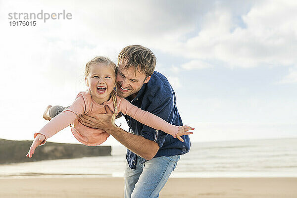 Glücklicher Vater spielt mit Tochter am Strand