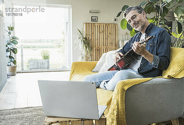 Mann spielt Gitarre und schaut sich zu Hause das Tutorial auf dem Laptop an