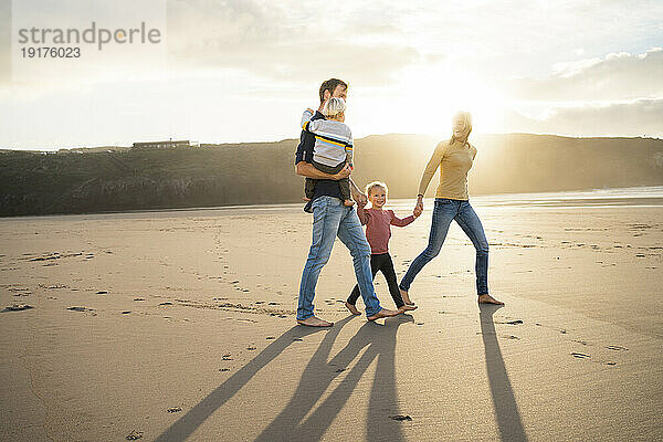Vater und Mutter gehen mit Kindern an einem sonnigen Tag am Strand spazieren
