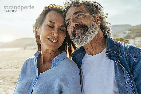 Lächelnde ältere Frau umarmt Mann am Strand an einem sonnigen Tag