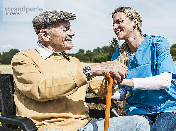 Glücklicher Mitarbeiter im Gesundheitswesen  der mit einem älteren Mann spricht  der im Rollstuhl sitzt
