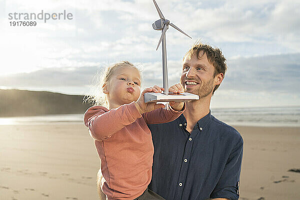 Lächelnder Vater und Tochter halten Windturbinenmodell unter bewölktem Himmel