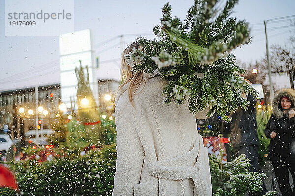 Blonde Frau trägt Weihnachtsbaum auf dem Markt