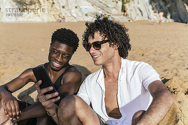 Lächelnder Mann teilt Smartphone mit Freund am Strand