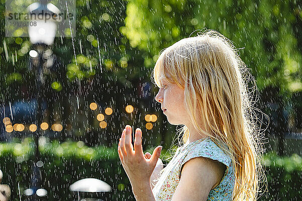 Blond girl enjoying fountain water falling in park