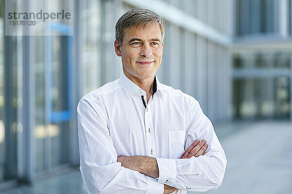 Casual businessman standing in front of office building with arms crossed