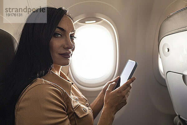 Schöne Frau mit Mobiltelefon im Flugzeug