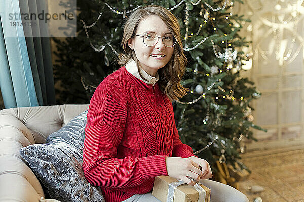 Lächelnde Frau verpackt Weihnachtsgeschenk auf Sofa zu Hause