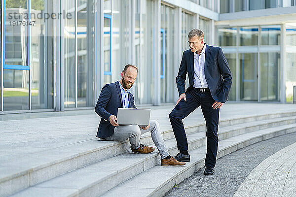 Zwei Geschäftsleute arbeiten gemeinsam am Laptop auf den Stufen eines Bürogebäudes