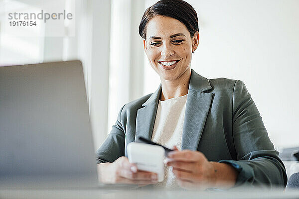 Lächelnde Geschäftsfrau benutzt Kreditkarte am Arbeitsplatz