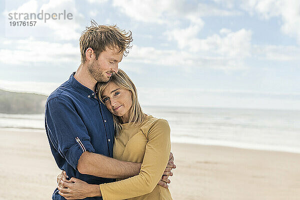 Glücklicher Mann umarmt Frau am Strand