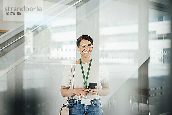 Lächelnde Geschäftsfrau mit Smartphone am Arbeitsplatz