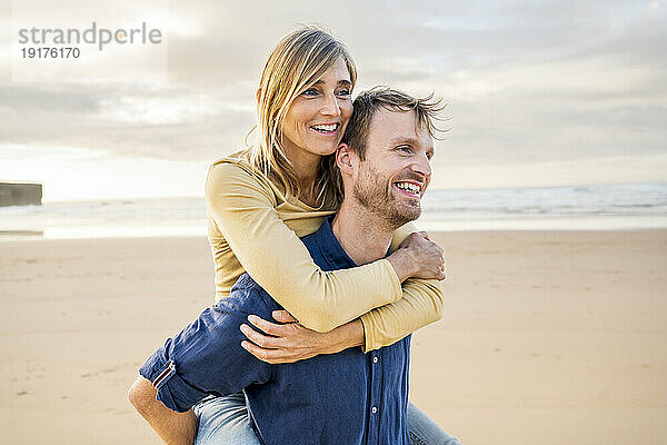 Glücklicher Mann gibt Frau am Strand Huckepackfahrt