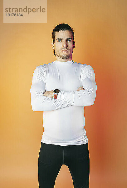 Man with arms crossed standing against orange background