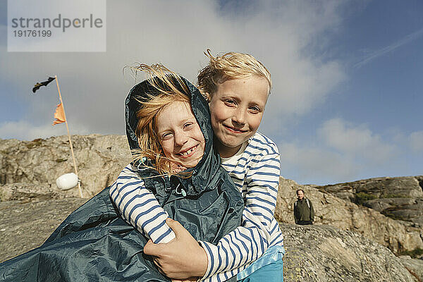 Lächelnder Junge umarmt Schwester an sonnigem Tag