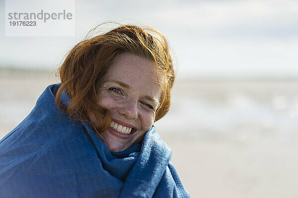 Glückliche Frau in Schal gehüllt am Strand