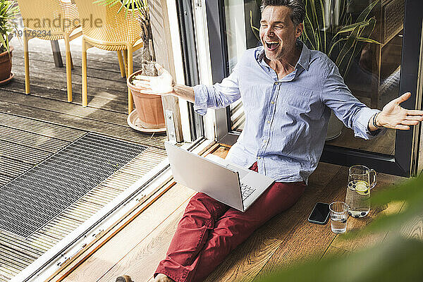 Porträt eines glücklichen Mannes mit Laptop am offenen Balkon