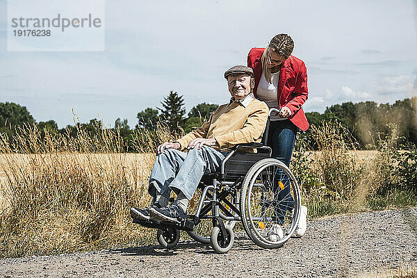 Frau schiebt älteren Mann mit Behinderung im Rollstuhl