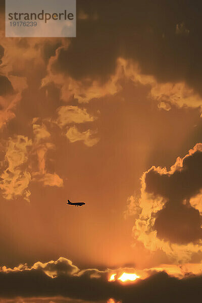 Silhouette eines Verkehrsflugzeugs  das bei Sonnenuntergang gegen den stimmungsvollen Himmel fliegt