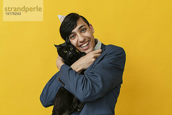 Glücklicher Mann umarmt Katze vor gelbem Hintergrund