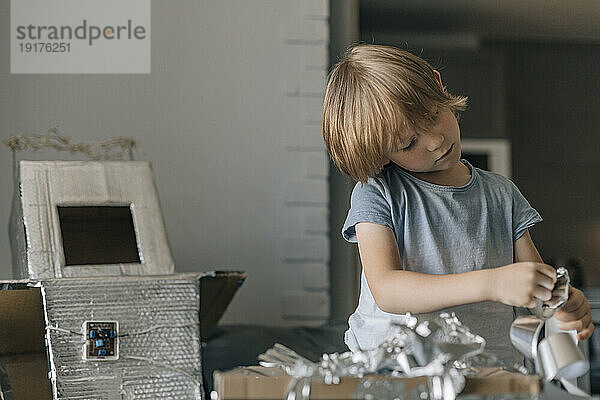 Konzentrierter Junge mit Silberfolienpapier bastelt Astronautenkostüm