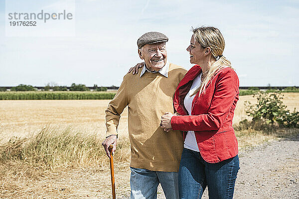 Lächelnder älterer Mann geht an einem sonnigen Tag mit einer Frau durch das Feld