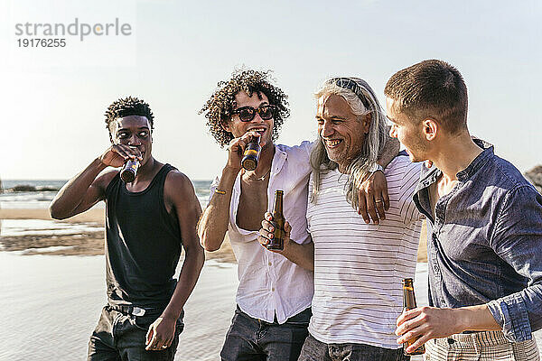 Fröhliche multiethnische Freunde  die Bier trinken und ihre Freizeit am Strand verbringen