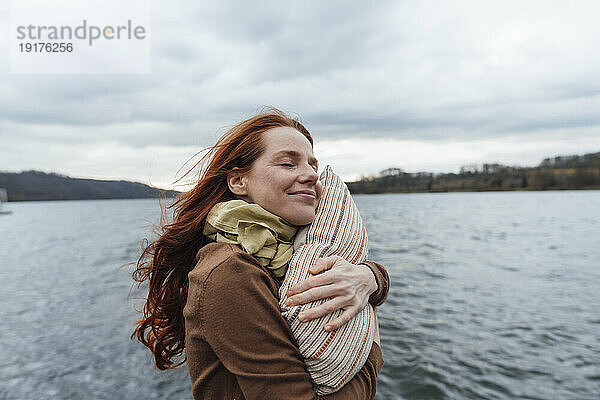 Lächelnde Frau umarmt Kissen am See
