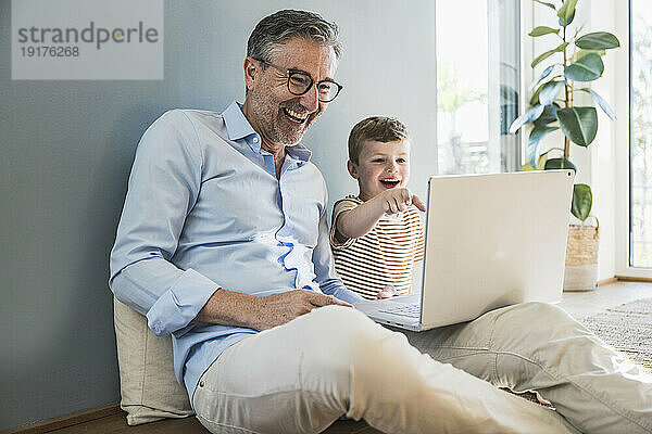 Glücklicher Großvater benutzt Laptop mit Enkel im Wohnzimmer