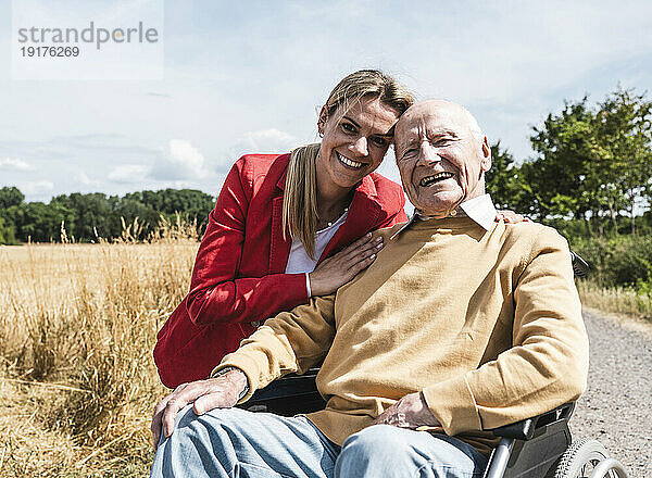 Glückliche Frau mit älterem Mann  der an einem sonnigen Tag im Rollstuhl sitzt