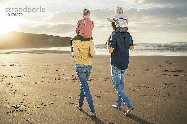 Mutter und Vater tragen Kinder auf Schultern am Strand