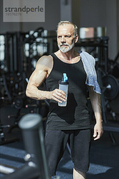 Nachdenklicher Mann mit Wasserflasche im Fitnessstudio