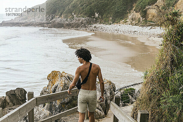 Shirtless man walking near railing at beach
