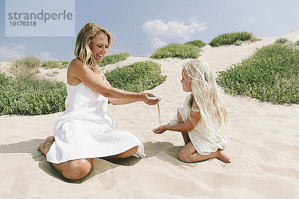 Glückliche Mutter und Tochter spielen an einem sonnigen Tag mit Sand am Strand