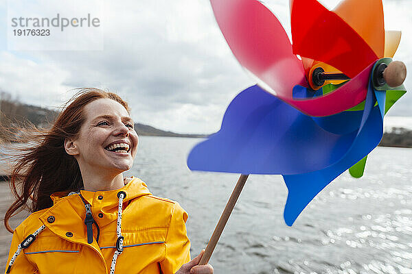 Fröhliche Frau mit Windradspielzeug am See