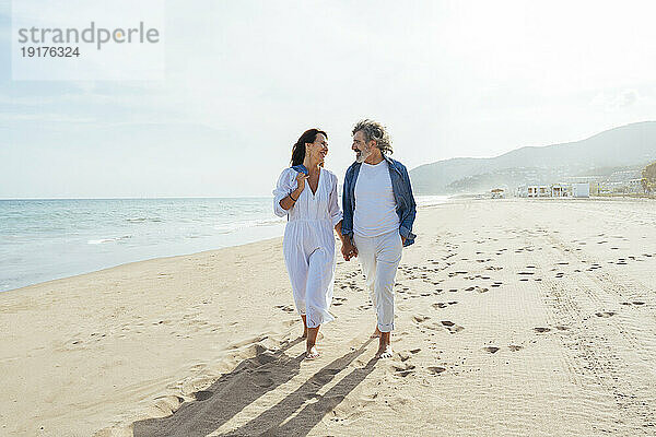 Lächelnde ältere Männer und Frauen  die an einem sonnigen Tag am Strand spazieren gehen