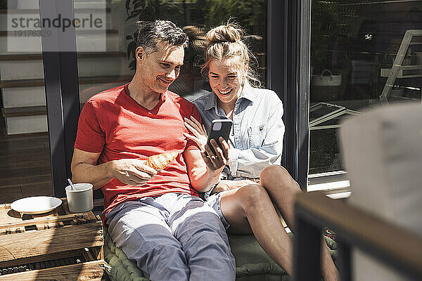 Paar entspannt sich mit Smartphone auf dem Balkon