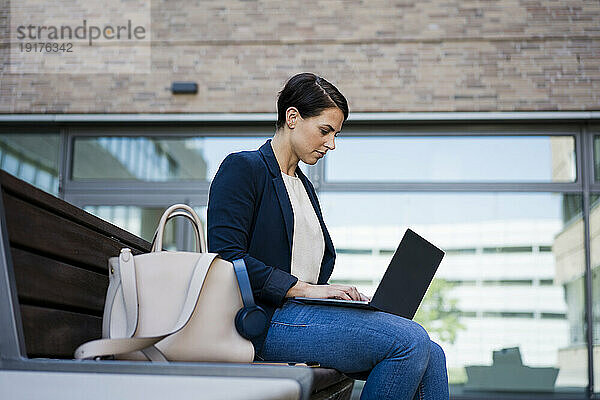 Konzentrierte Geschäftsfrau benutzt Laptop und sitzt auf Bank