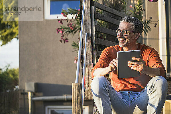 Glücklicher Mann mit Tablet-PC sitzt auf Stufen
