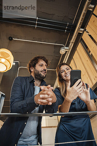 Lächelnde Geschäftsfrau zeigt Geschäftsmann im Büro Smartphone