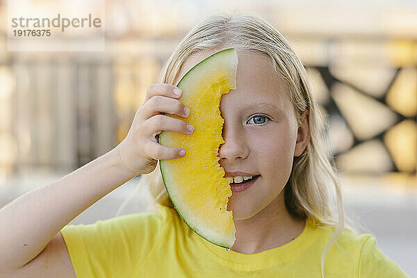 Lächelndes Mädchen  das ihr Gesicht mit gelber Wassermelone bedeckt