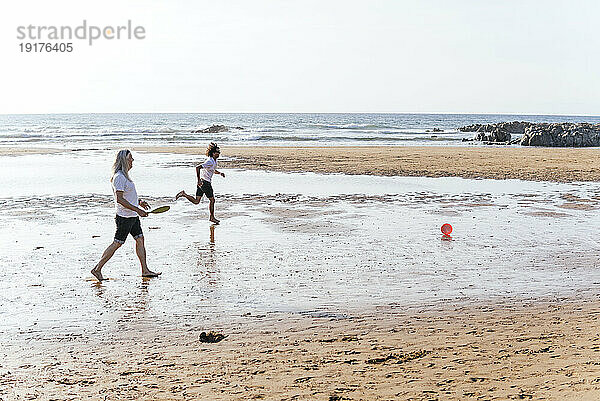 Friends running behind plastic disc at beach on sunny day