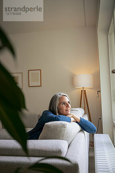 Nachdenkliche reife Frau sitzt zu Hause auf dem Sofa
