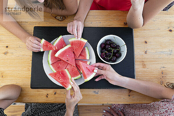Freunde essen Wassermelone und Kirschen am Tisch