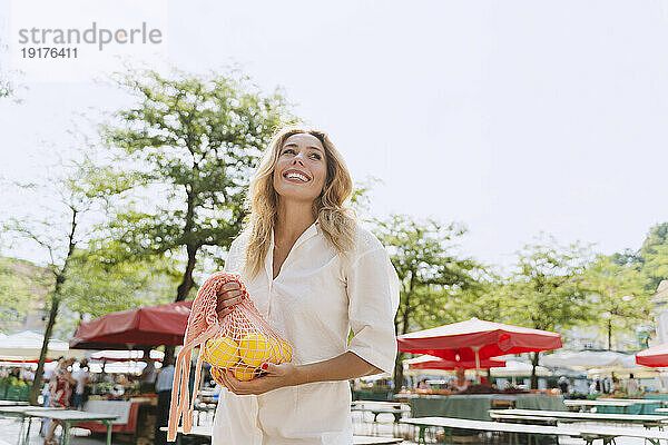 Glückliche Frau hält eine Tüte Zitronen auf dem Markt