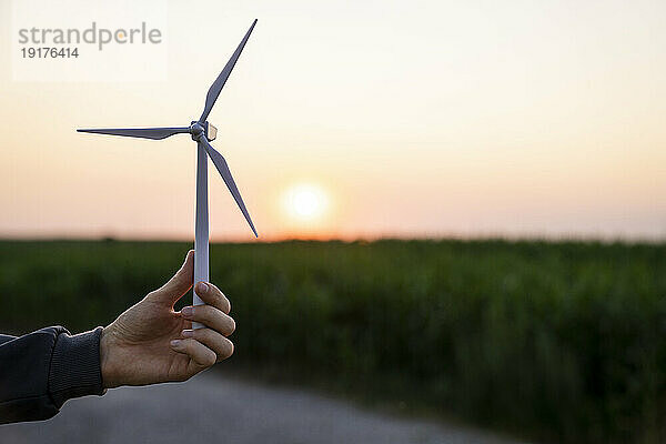 Hand eines Ingenieurs mit Modell einer Windkraftanlage bei Sonnenuntergang