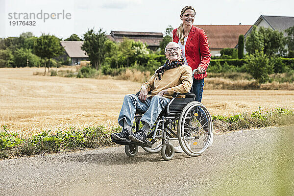 Lächelnde Frau schiebt älteren Mann im Rollstuhl